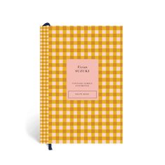 a yellow and white checkered notebook with a pink label on the front, sitting in front of a white background