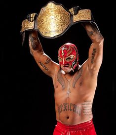 a man in red trunks holding up a gold wrestling belt with tattoos on his chest