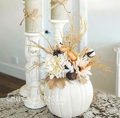 a white pumpkin decorated with flowers and two candles