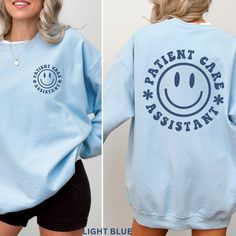 a woman wearing a blue sweatshirt with the words patient care assistant printed on it and smiling