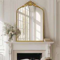 a mirror sitting on top of a fireplace next to a vase with flowers in it