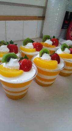 small dessert cups with fruit and whipped cream on them sitting on a counter in a kitchen