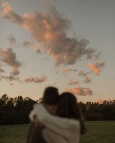 a man and woman embracing each other while the sun is setting in the sky behind them