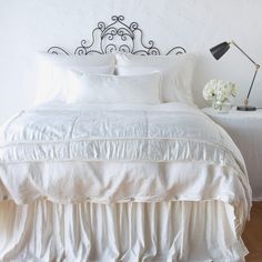 a bed with white linens and pillows in a small room next to a lamp