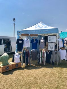 a tent with shirts and t - shirts on display in front of it at an outdoor event