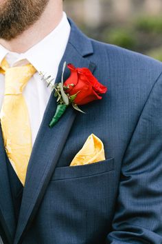 a man wearing a blue suit and yellow tie with a red rose in his lapel