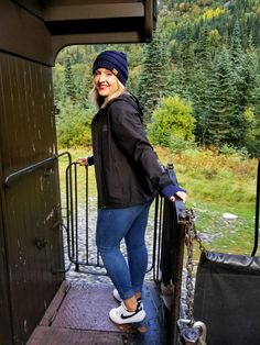 a woman standing on the side of a train with her hands in her pockets and looking at the camera