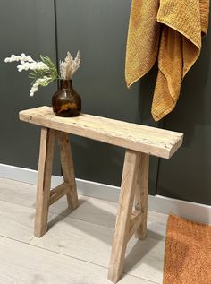 a wooden bench sitting next to a towel and vase on top of a table in front of a green wall