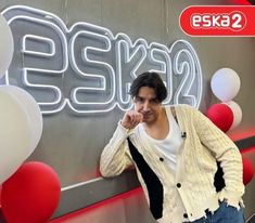 a man standing in front of a sign with balloons around him and pointing at the camera