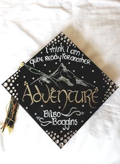 a black and gold graduation cap with the words adventure written in cursive writing