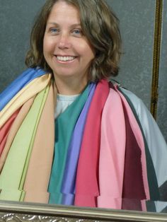 a woman is smiling and holding several different colored scarves