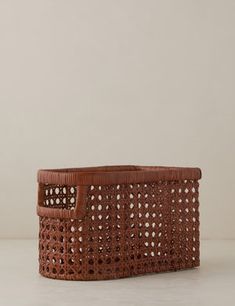 a brown basket sitting on top of a white table next to a planter with holes in it