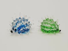 two different colored glass balls sitting next to each other on a white surface, one is green and the other is blue