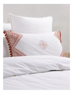 a bed with white sheets and orange pillows