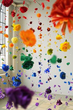 colorful paper flowers hanging from the ceiling in front of a white wall with windows and curtains