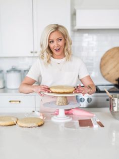 a woman standing in front of a cake on top of a white counter next to cookies