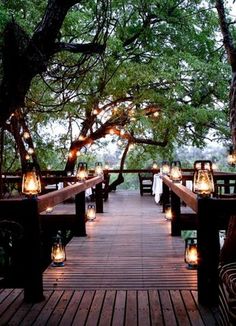 an outdoor dining area with lanterns and lights on the wooden walkway leading up to trees