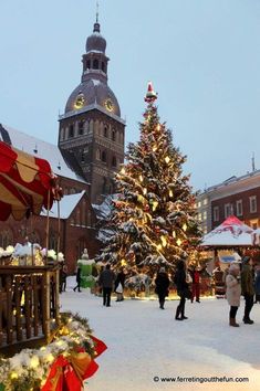 people are walking around in the snow near a christmas tree with lights and decorations on it