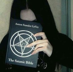 a woman with long black hair holding up a book in front of her face and looking at the camera