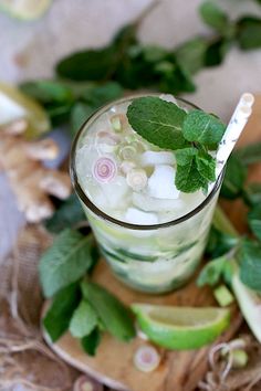 a glass filled with ice and mint sitting on top of a wooden plate next to sliced apples