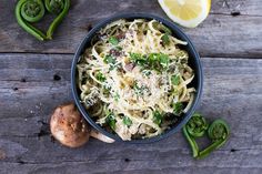 a bowl filled with pasta next to sliced green peppers and lemon wedges on top of a wooden table