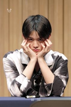 a young man sitting at a table with his hands on his face