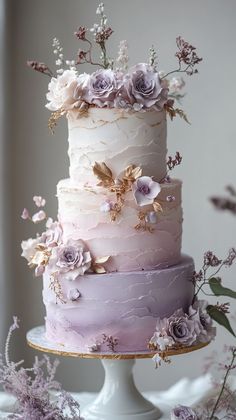 a three tiered cake with purple flowers on top and white frosting in the middle