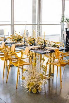 a dining room table set with yellow chairs and centerpieces, surrounded by greenery