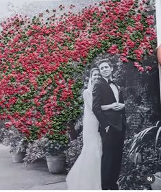 a wedding photo is being held up in front of a wall with flowers on it