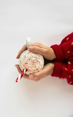 two hands holding a cup with whipped cream and candy canes in it, on a white background