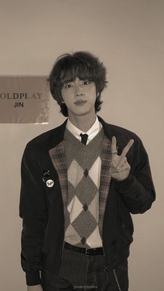 a young man wearing a sweater and tie making the peace sign with his hand in front of him