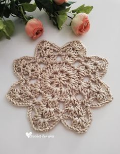 a crocheted doily with roses on the side and one flower laying next to it