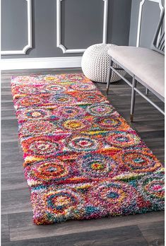 a multicolored area rug with a bench in the corner and gray walls behind it