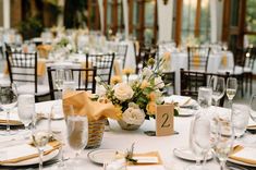 Image shows a white, yellow and green floral centerpiece next to a table number 2 and the table features yellow and green accent decor, in the wedding reception space of the New England Botanic Garden at Tower Hill. Wedding Floral Centerpieces