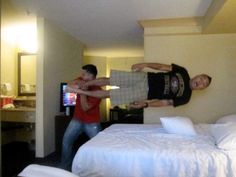 two men in a hotel room playing video games on the bed and another man standing next to him