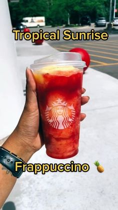 a person holding up a drink with the words tropical sunrise frapuccino on it