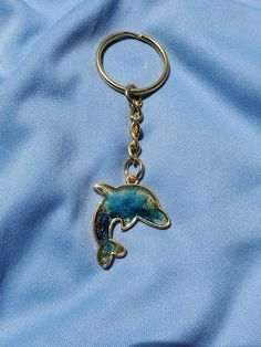 a dolphin keychain is on top of a blue cloth with a gold chain