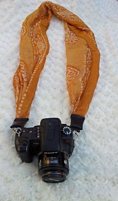 the camera is sitting next to an orange scarf on top of a white carpeted floor