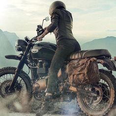 a man riding on the back of a motorcycle down a dirt road with mountains in the background