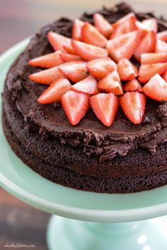 a chocolate cake topped with sliced strawberries on top of a green plate and wooden table