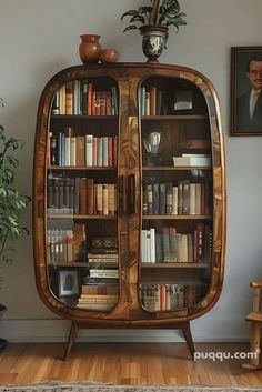 a bookcase with many books in it next to a potted plant and pictures on the wall