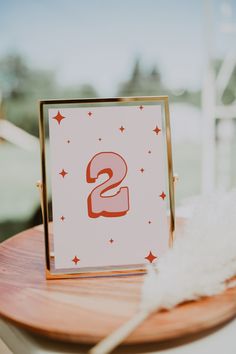 a wooden table topped with a white and red sign next to a feather on top of it