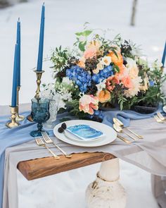 the table is set with blue and orange flowers, gold candles, and silverware