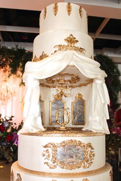 a large white and gold wedding cake with pictures on the top, surrounded by flowers