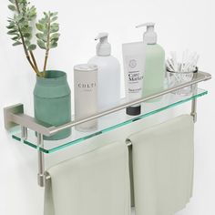 a glass shelf with towels, soap and lotion on it next to a potted plant