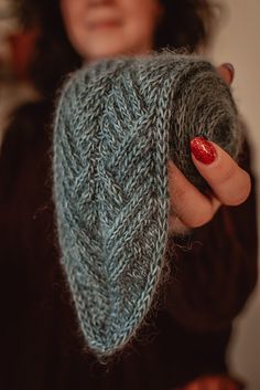 a woman holding up a knitted object in one hand and a red manicure on the other