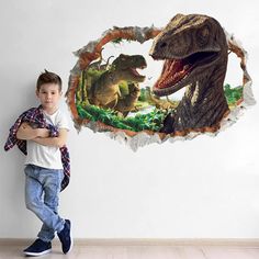 a young boy standing in front of a dinosaur wall decal