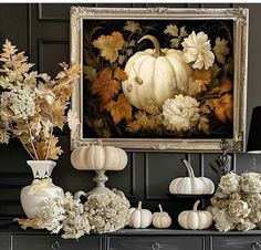 an arrangement of flowers and pumpkins on a mantle in front of a framed painting