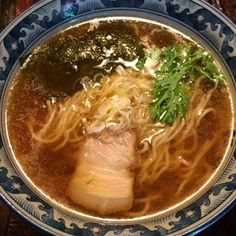 a blue and white bowl filled with noodles, meat and veggies on top of a wooden table