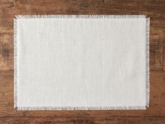 a white place mat with fringes on a wooden surface